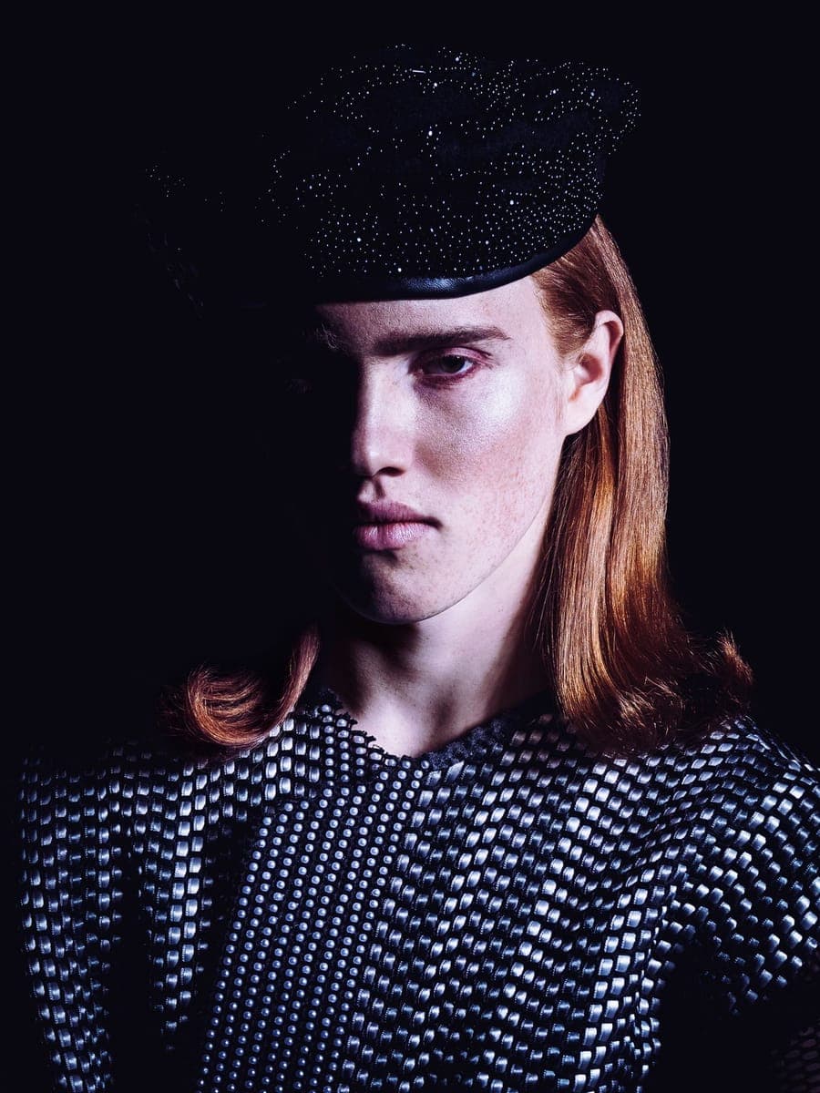 Red-haired model in a sparkling black hat and studded dark dress, half in shadow