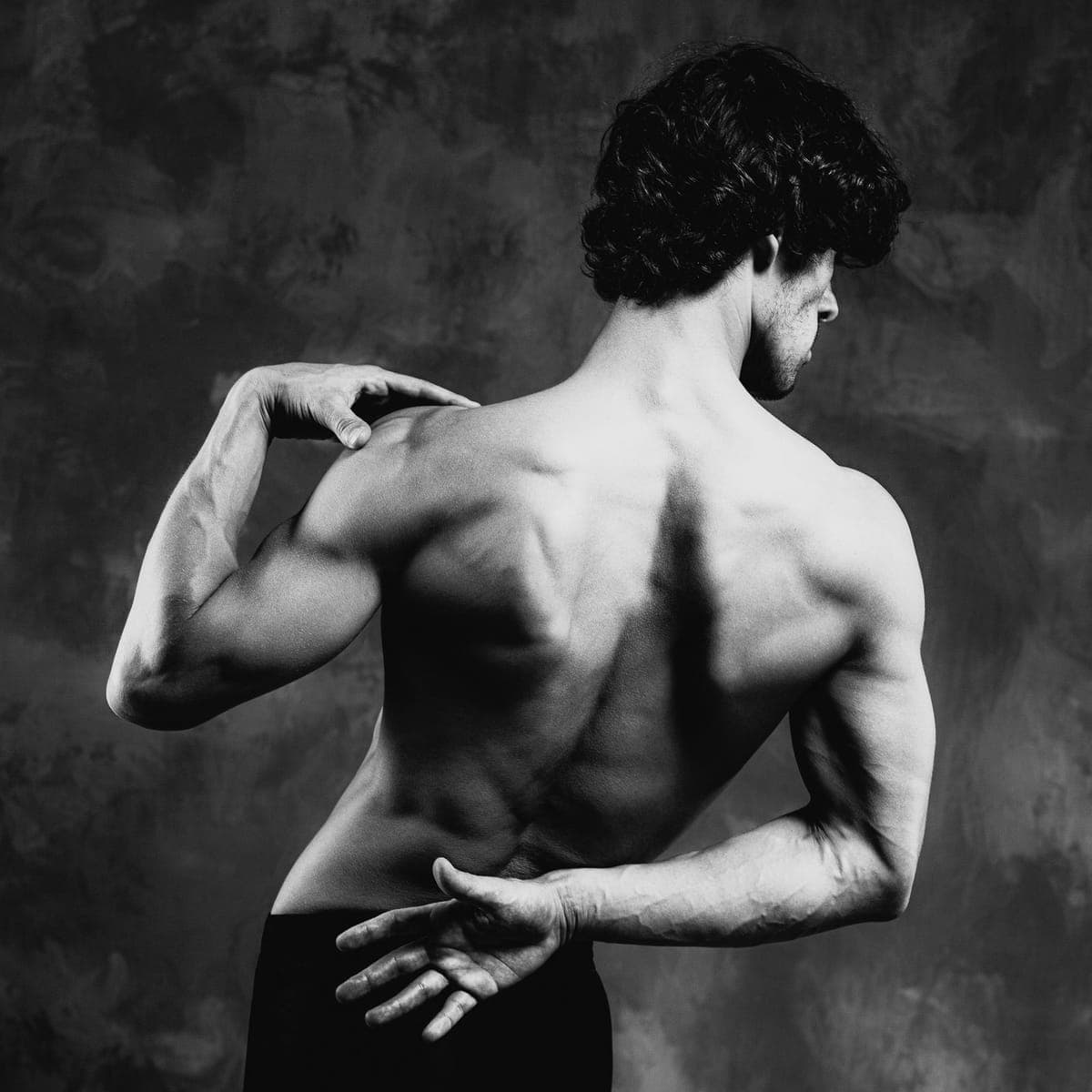 Bare back turned to the camera, one hand at the shoulder, the other folded behind the waist