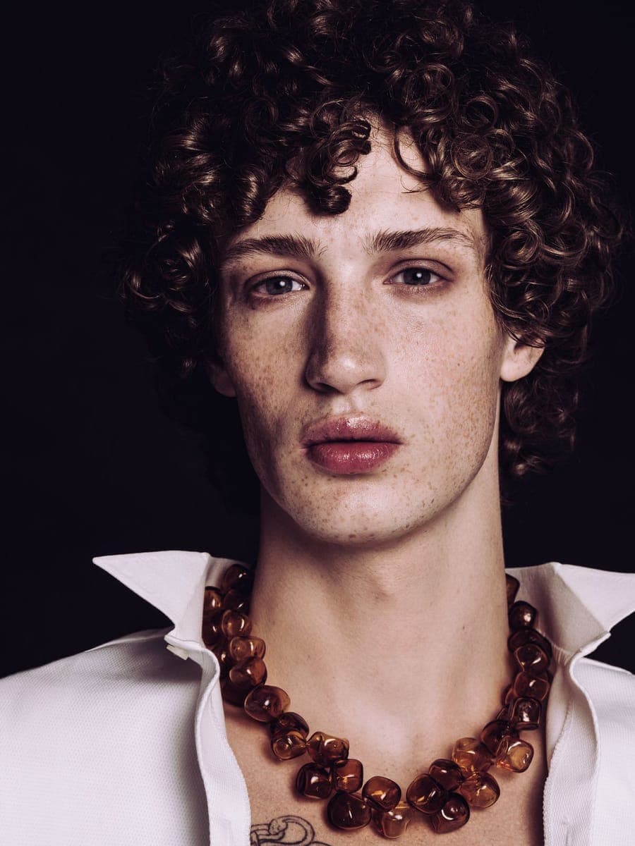 Freckled sitter under copper curls in an open white shirt and a heavy amber necklace